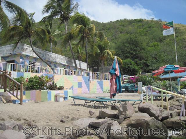 Flag of St Kitts and Colorful wall and building at Monkey Bar Beach in St Kitts.jpg
